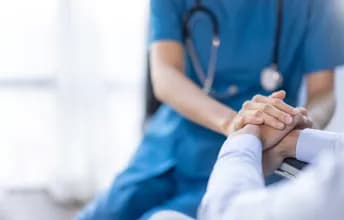 Profissional da saúde segura a mão de um paciente, representa o compromisso institucional com a qualidade, segurança e atuação no SUS, promovendo um atendimento humanizado e eficaz para todos.