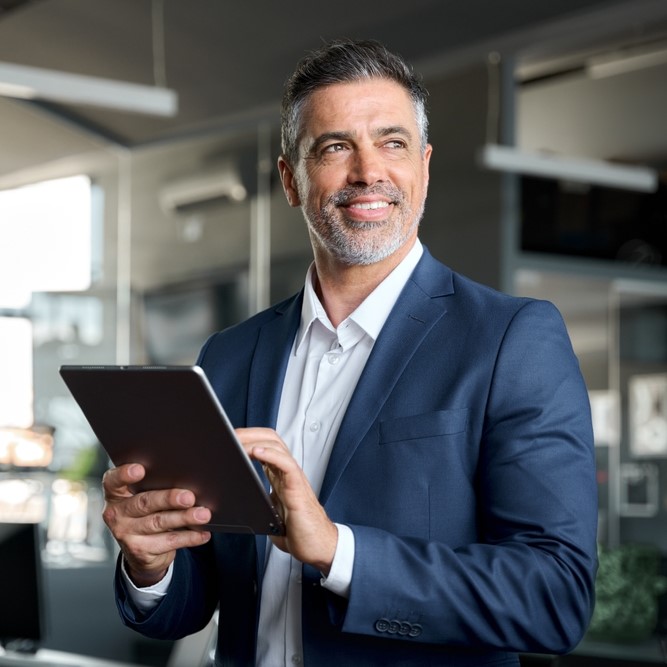 Executivo sorridente usando tablet em ambiente corporativo, representa oportunidades de carreira no Einstein, liderança e vagas disponíveis em recursos humanos em programa 'Trabalhe Conosco'.